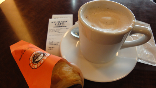 a cup of foamy coffee and a croissant in a wrapper
